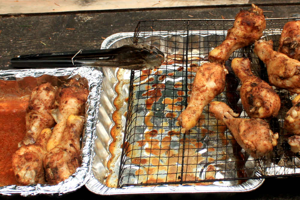 Precooked chicken drumsticks, with tender skin, being transferred from the pan to the smoker rack.