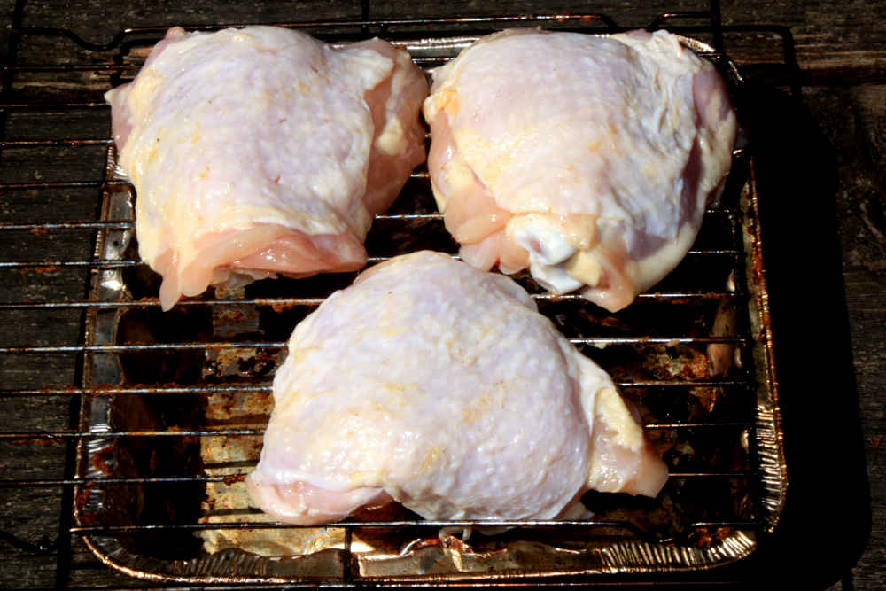 Three chicken thighs with the fat-scraped skins put back in place, ready for seasoning and smoking.